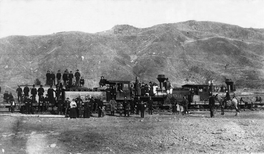 One b/w photograph of trains from the Denver and Rio Grande Railroad, first train into Aspen. A large group of people is posed around the trains, including women and children. (according to the Aspen Daily Times, the railroad arrived on October 28, 1887, and a grand celebration was held a few days later)