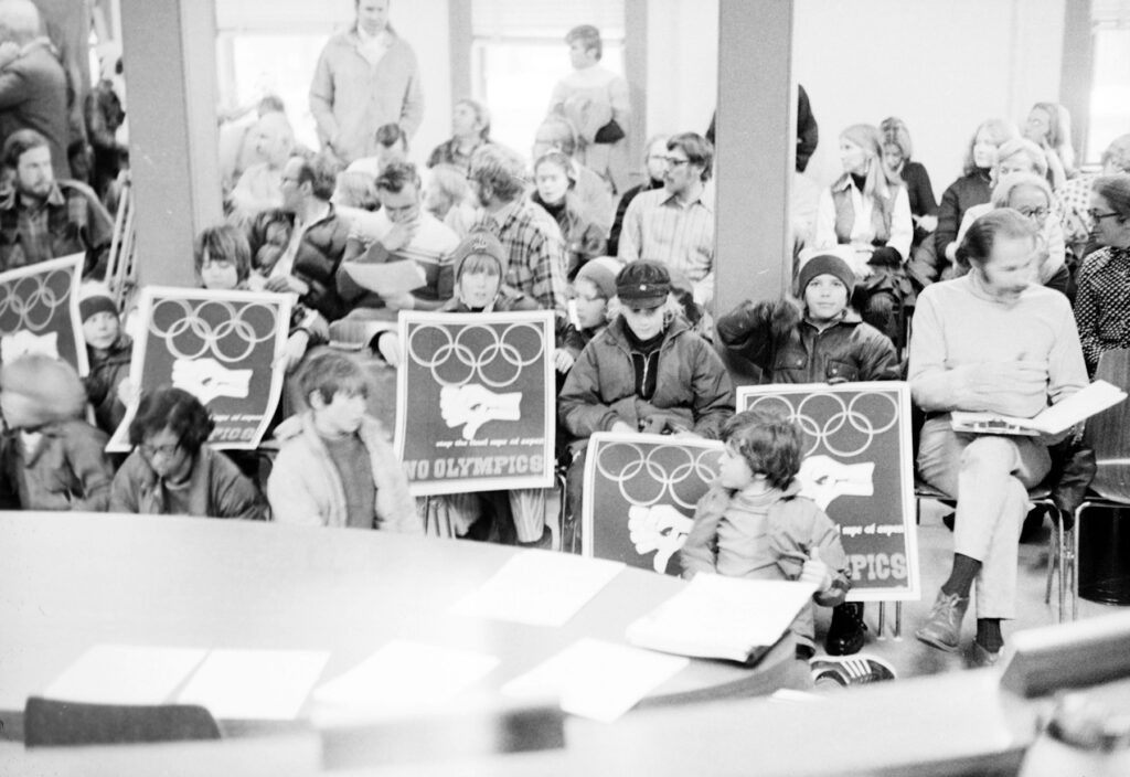 One b/w film negative of a group of people gathered to protest the possibility of the Olympics coming to Colorado, January 1972. Bil Dunaway is sitting on the far right and many people are holding protest posters made by Tom Benton. The opposition to the Olympics was a reaction to the rapid growth in Colorado at the time.