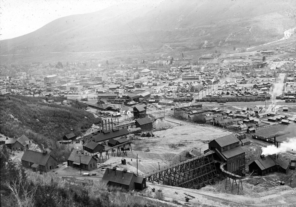 One lantern slide of the Durant Mine and a panoramic view of the edge of Aspen Mountain, the mine and east Aspen and Red Mountain. Original Street and Ute Avenue can be seen, as well as the railroad tracks with cars on it. Hunter Creek is in the far right background, as well as Red Mountain.