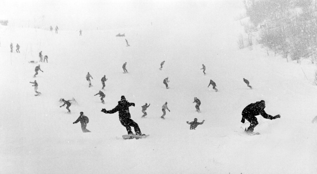 One b/w photograph of a group of snowboarders making their way down Tiehack during a snowboarding demonstration, 1986. The photo is in the December 4, 1986 Aspen Times, p. 7C. *This was likely part of of filming for "Snowboard Meltdown."