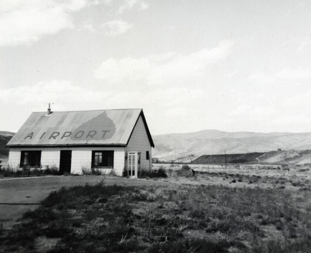 One b/w photograph of a small building with "Airport" written on roof, and a large Aspen leaf, 1960.