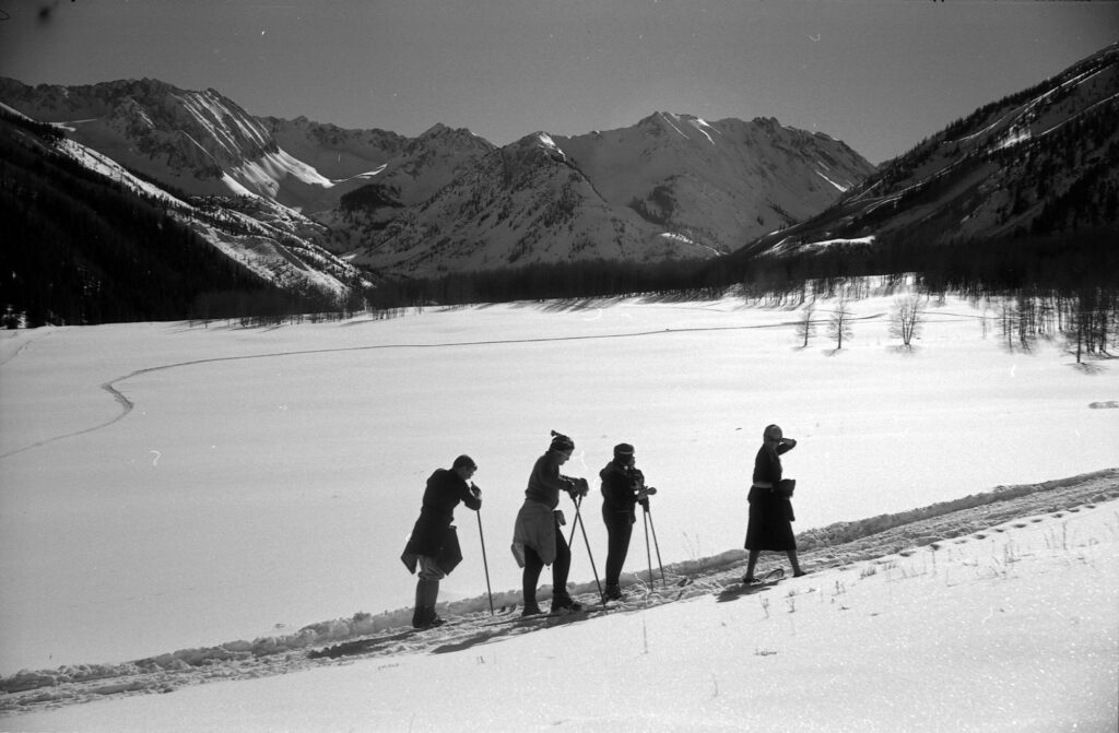 One b/w negative of a group cross-country skiing and snowshoeing in Ashcroft, 1956. The woman in front in snowshoes is Elizabeth Paepcke. There are three men behind her on cross-country skis.