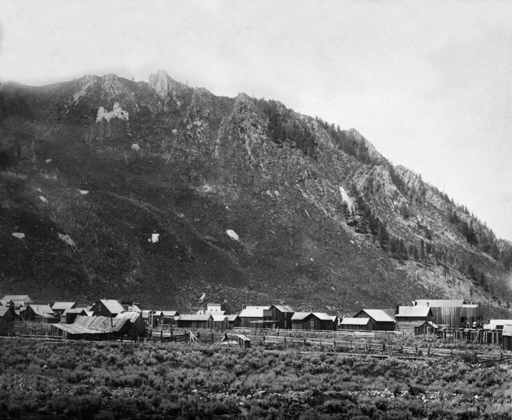One b/w photograph of early Aspen, with Aspen Mountain in the background. Several wooden buildings and fences are visible. 1882.