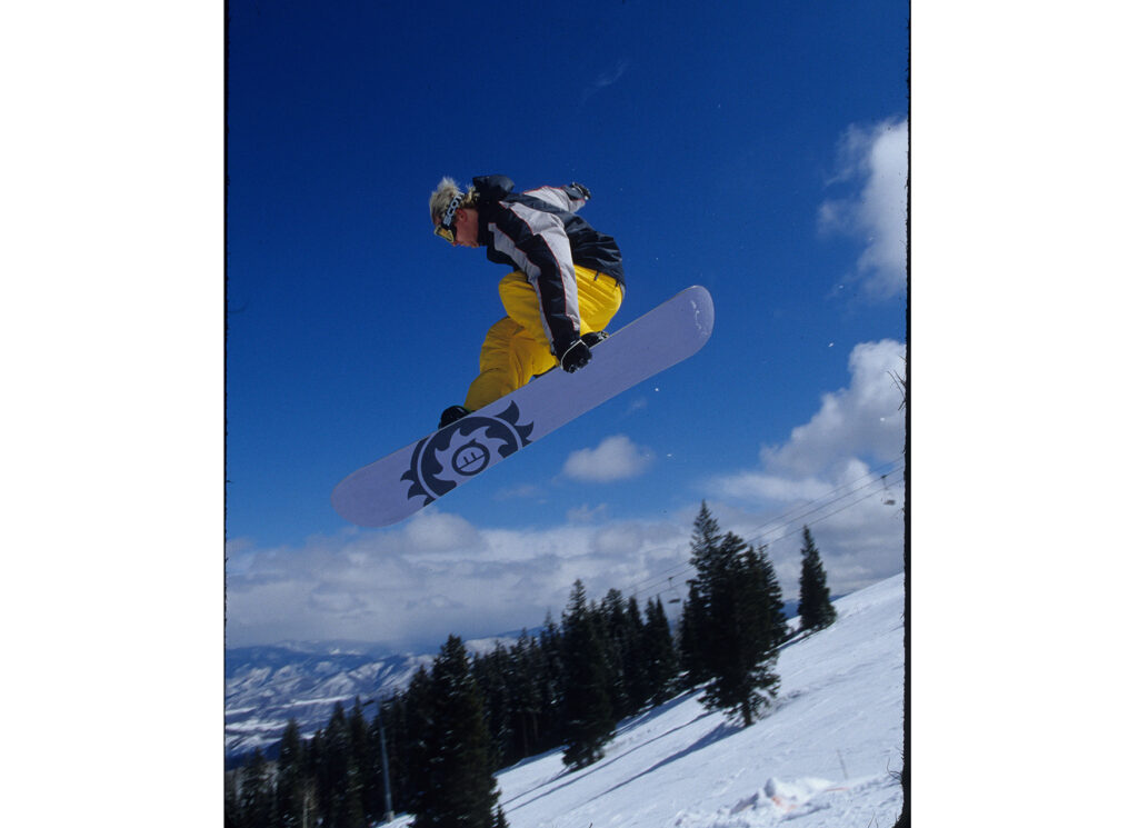One color slide of a man snowboarding at Snowmass, March 2002. He has gone off a jump.