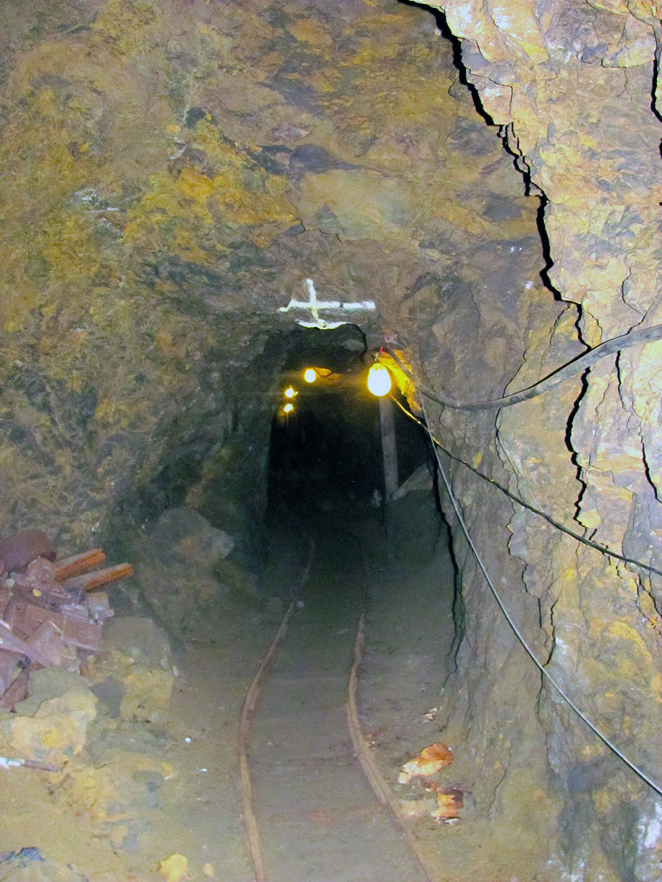 Color image looking into the tunnel of the the smuggler ming with cables along the right side for powering lights that light the tunnel, ore cart tracks lead into the tunnel as well.