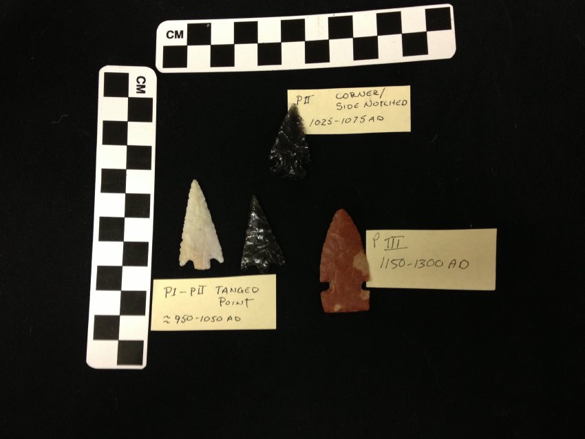 A color image of a four prehistoric replica arrowhead points (corner notched obsidian, two tanged points- one chert and one obsidian, and one red chert side notched point) ranging in dates from 950 AD to 1300 AD